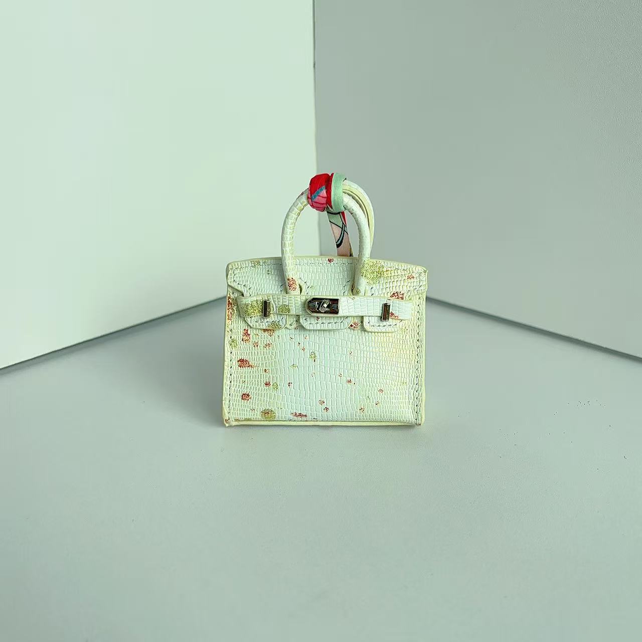 Front view of an off-white mini Birkin handbag charm featuring unique colorful speckle details and a silk scarf handle.