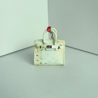 Front view of an off-white mini Birkin handbag charm featuring unique colorful speckle details and a silk scarf handle.