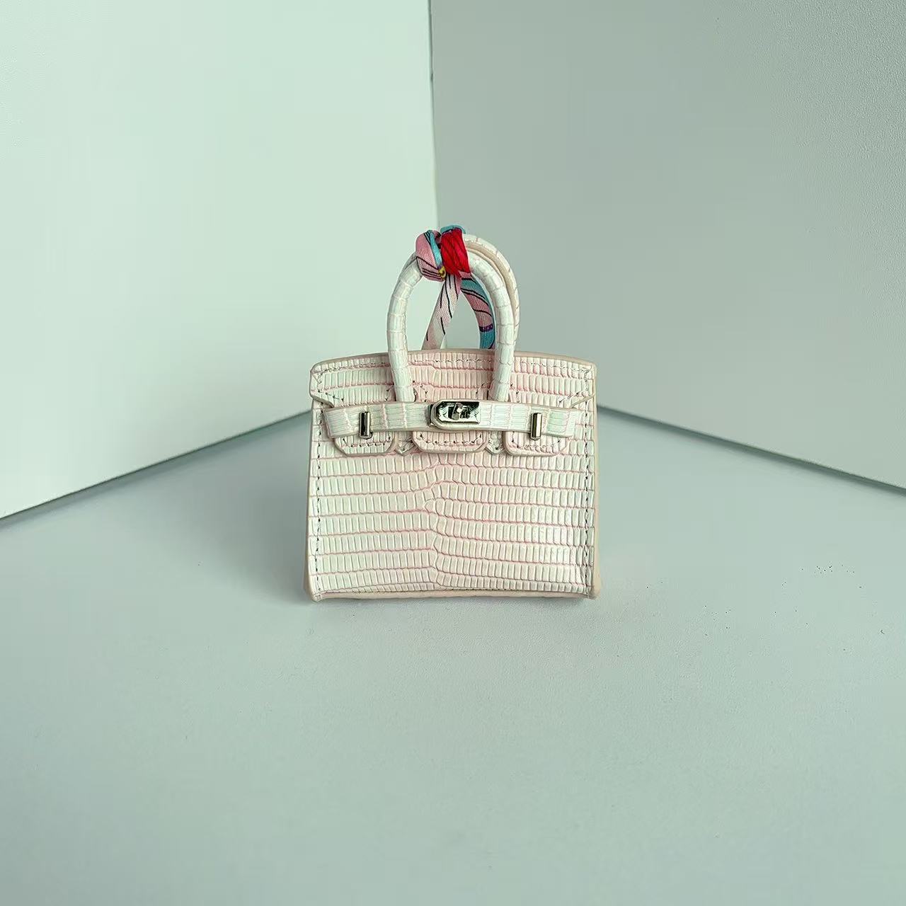 Front view of a pink gradient mini Birkin handbag charm featuring a luxury crocodile embossed texture and silk scarf handle.