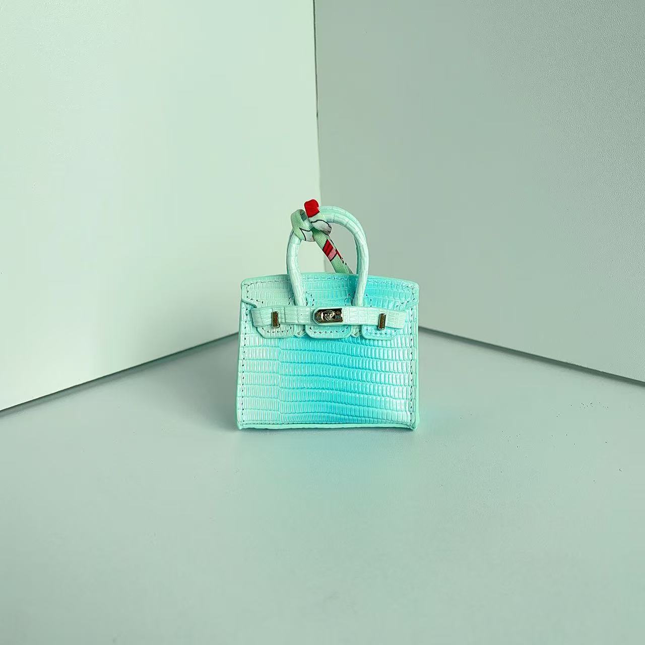 Front view of a Light Blue Gradient mini Birkin handbag charm featuring a luxury crocodile embossed texture and silk scarf handle.