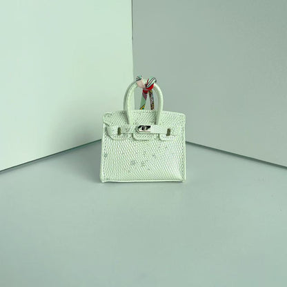 Front view of a White with Speckle mini Birkin handbag charm featuring a luxury crocodile embossed texture and silk scarf handle.