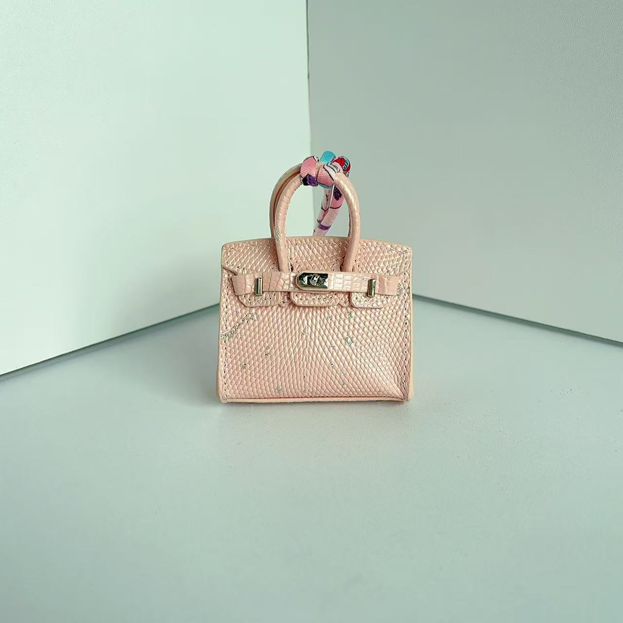 Front view of a Pink with Speckle mini Birkin handbag charm featuring a luxury crocodile embossed texture and silk scarf handle.