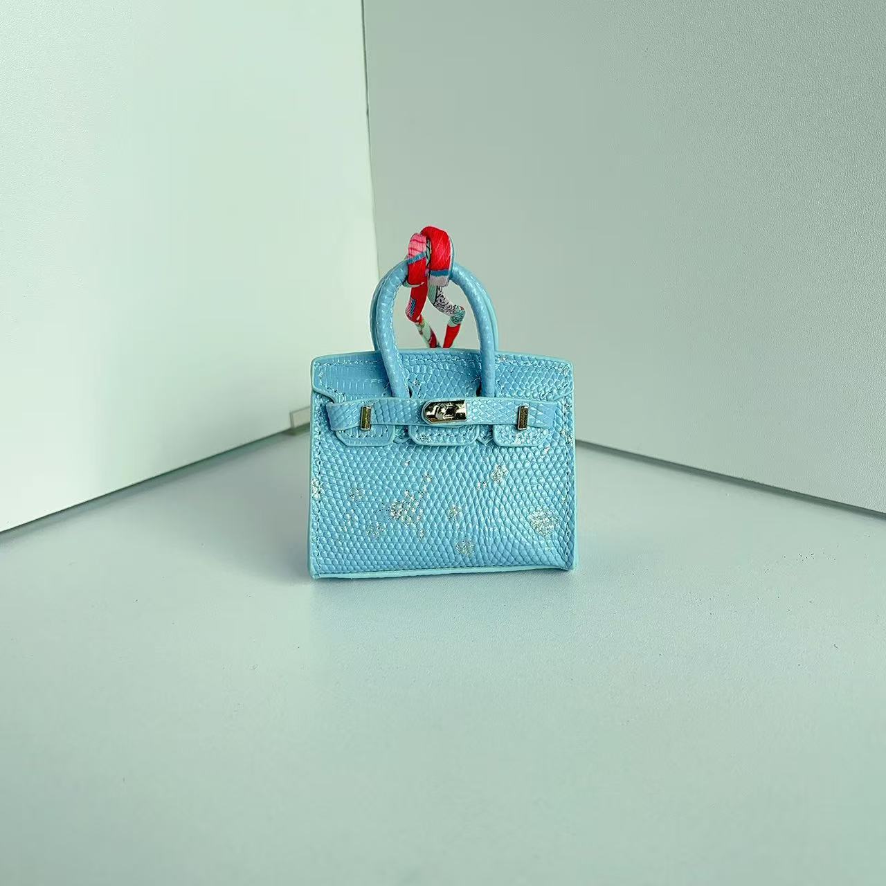 Front view of a Light Blue with Speckle mini Birkin handbag charm featuring a luxury crocodile embossed texture and silk scarf handle.
