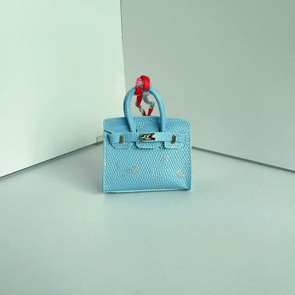 Front view of a Light Blue with Speckle mini Birkin handbag charm featuring a luxury crocodile embossed texture and silk scarf handle.
