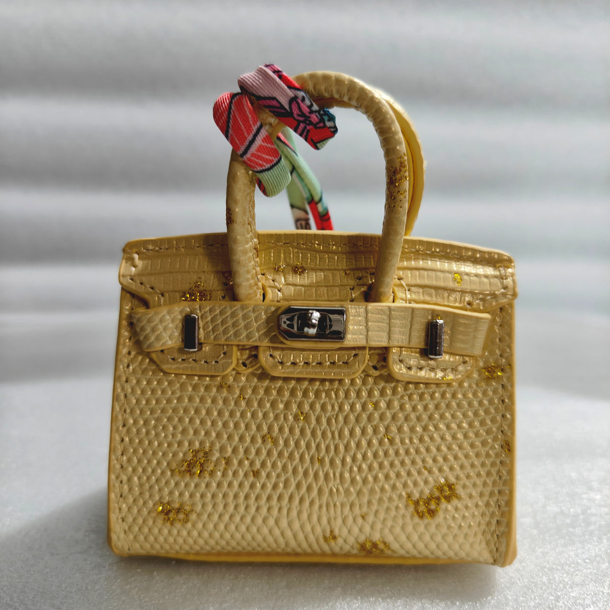 Front view of a Yellow with Speckle mini Birkin handbag charm featuring a luxury crocodile embossed texture and silk scarf handle.