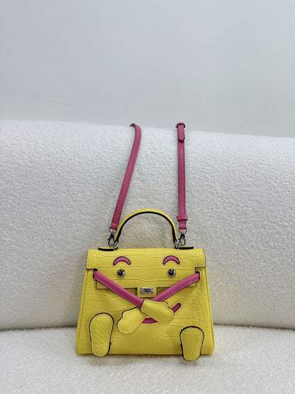 A two-tone yellow and pink leather doll bag, featuring a unique facial design and an adjustable shoulder strap.