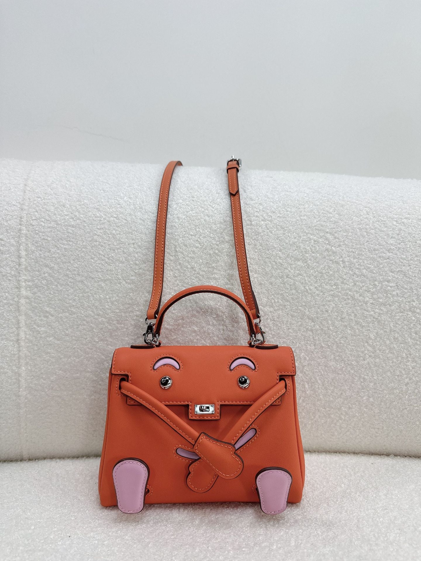  Unique orange and pink leather doll bag with quirky face design and adjustable strap.