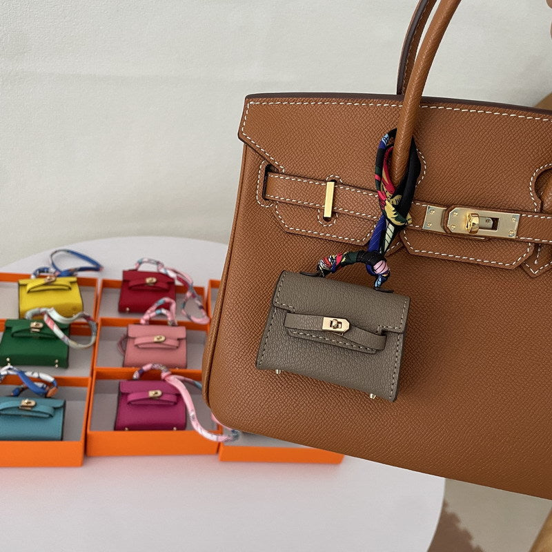 Gray mini Kelli handbag charm used as a stylish accessory on a brown bag, doubling as a vegan leather earphone case.