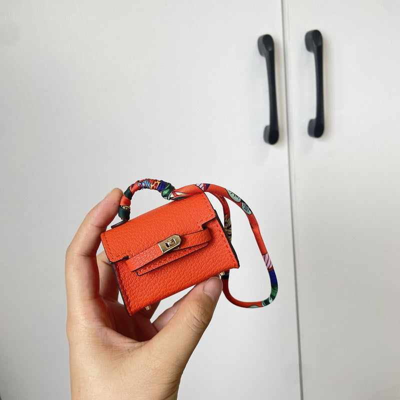 An orange mini Kelli bag charm—wrapped in a colorful silk scarf—serves as a vegan leather case for storing earphones.