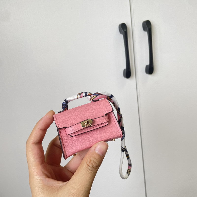 Handheld close-up of a pink mini Kelli handbag charm with a silk scarf handle, doubling as a vegan leather earphone storage case.