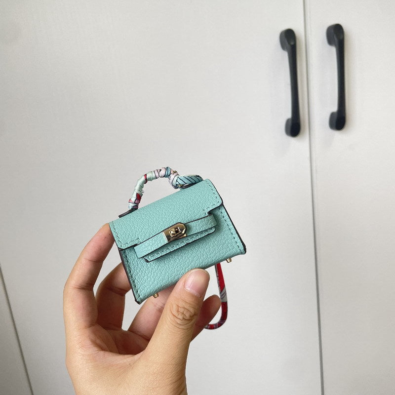 Handheld close-up of a light blue mini Kelli handbag charm with silk scarf detail, serving as a vegan leather earphone case.