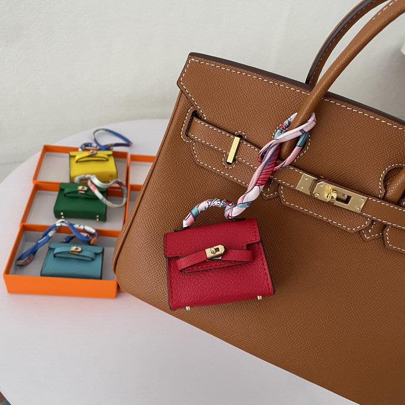 Red mini Kelli handbag charm with a silk scarf handle hanging on a brown tote bag, functioning as a vegan leather earphone case.