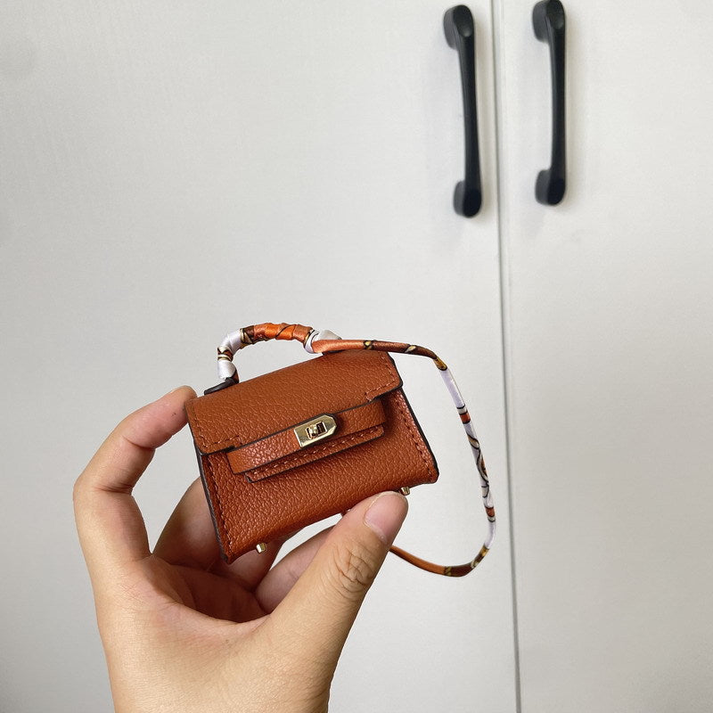 A caramel-colored Mini Kelli bag charm, featuring an orange silk scarf handle.