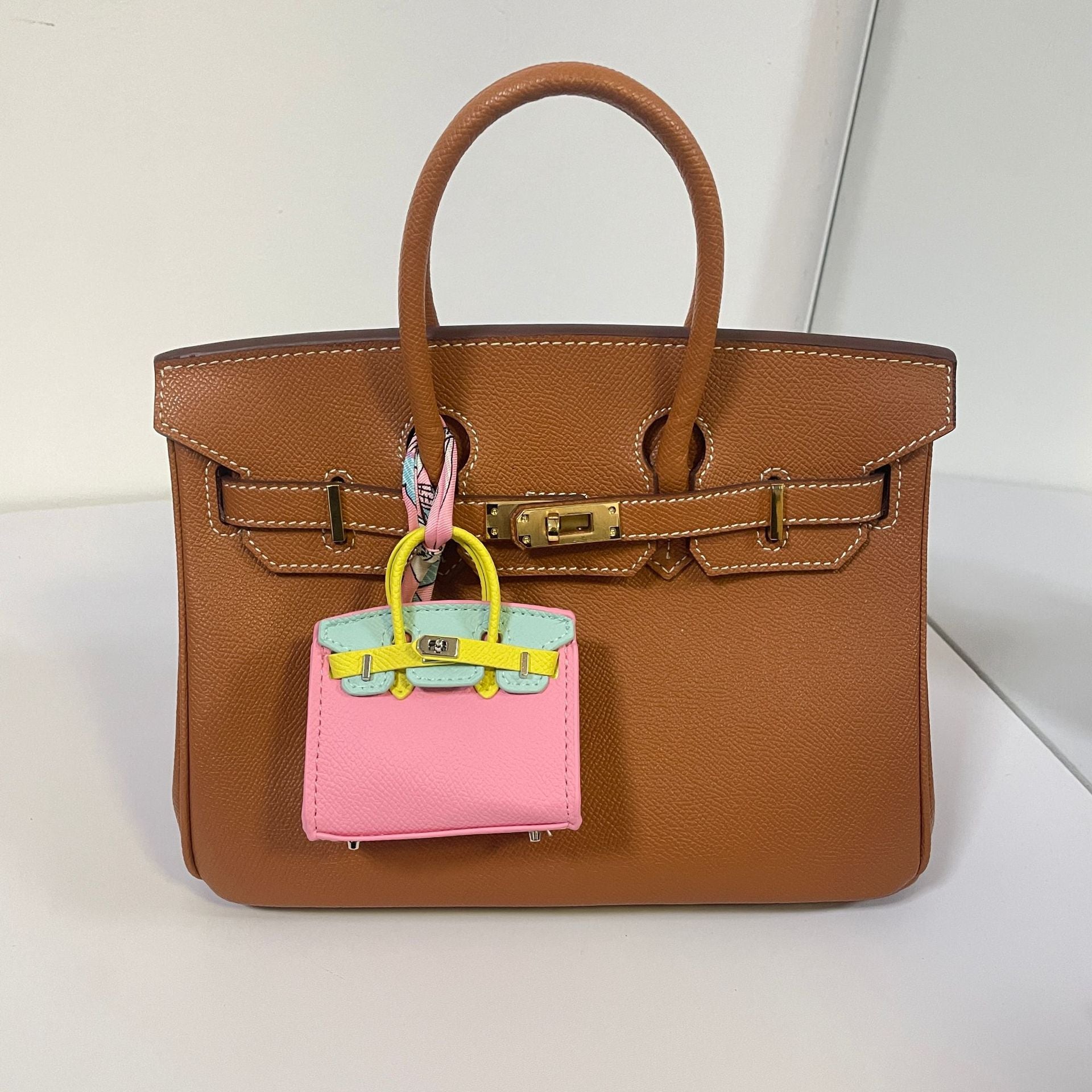 Tri-color pink, blue, and yellow mini Birkin bag charm on a brown handbag.