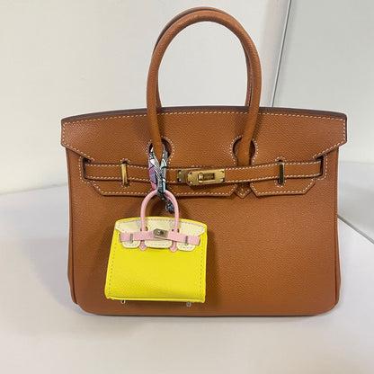 Tri-color yellow, pink, and white mini Birkin charm on a brown handbag.