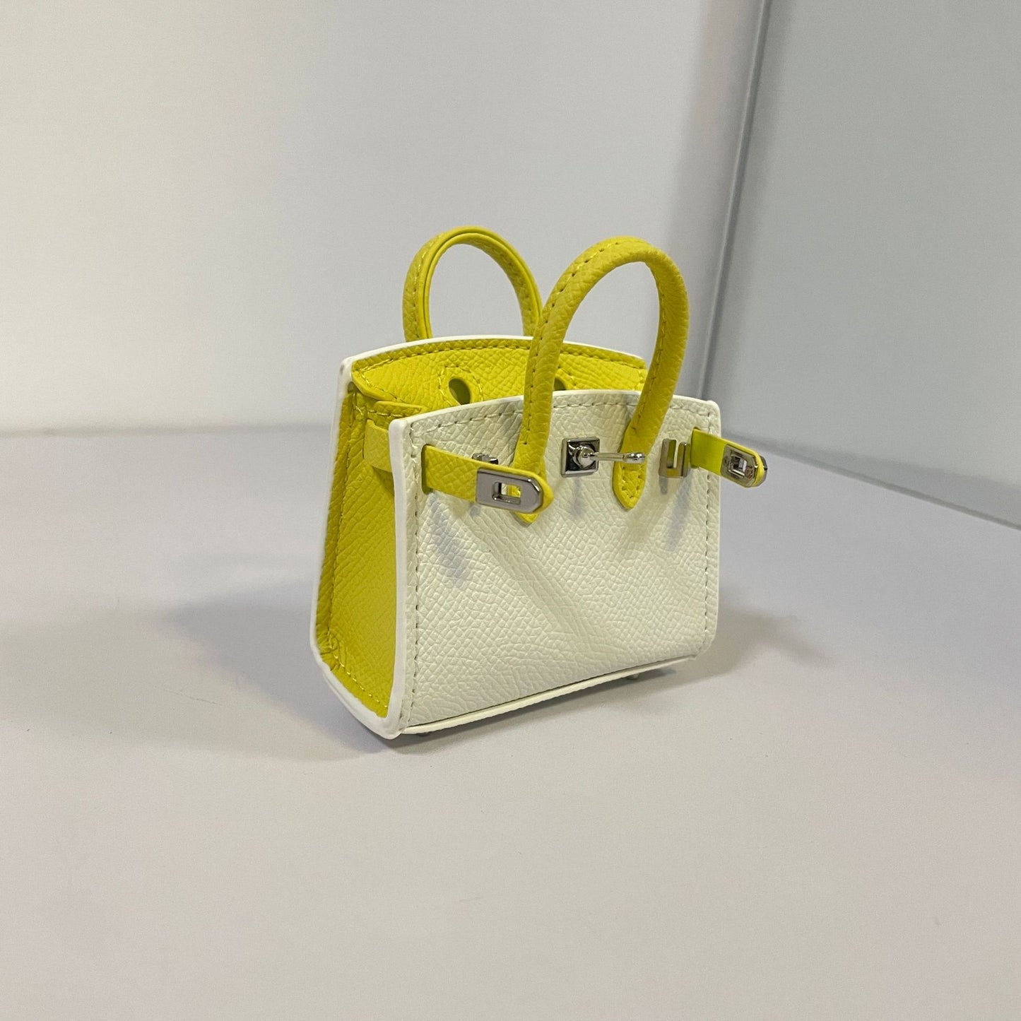 Two-tone white and yellow mini Birkin bag charm and AirPods holder.