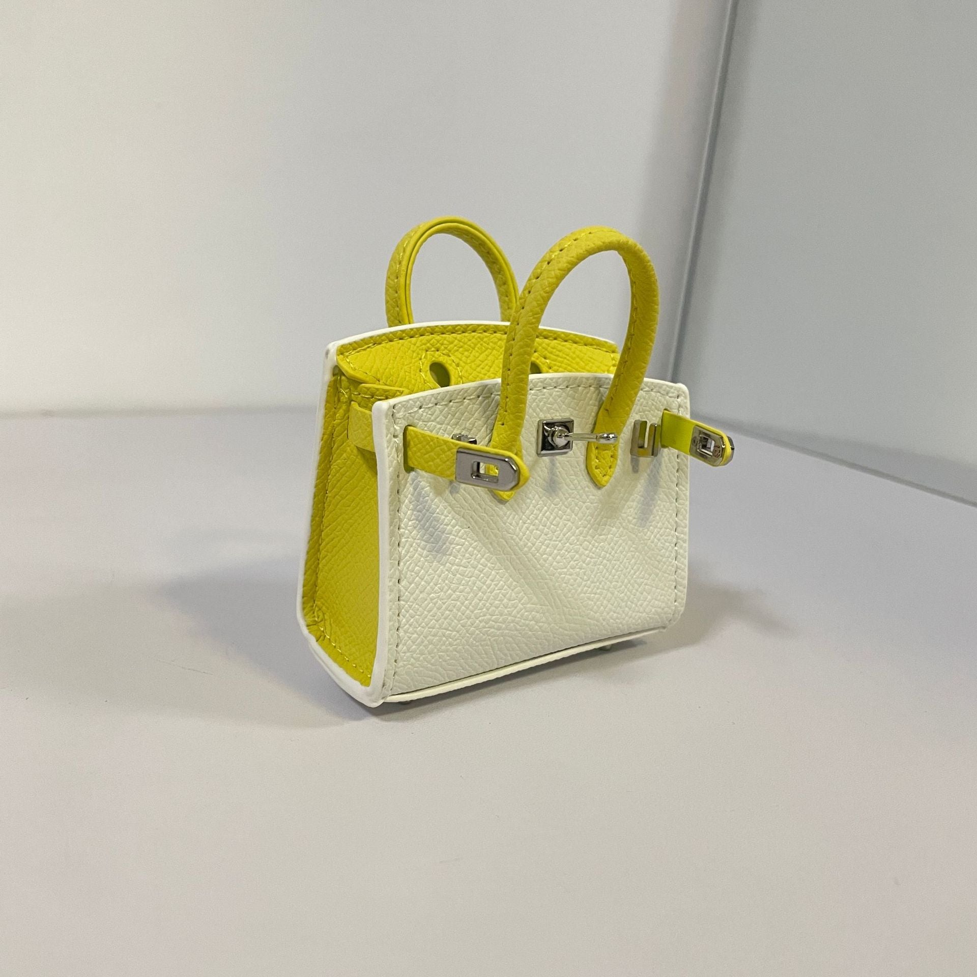 Two-tone white and yellow mini Birkin bag charm and AirPods holder.