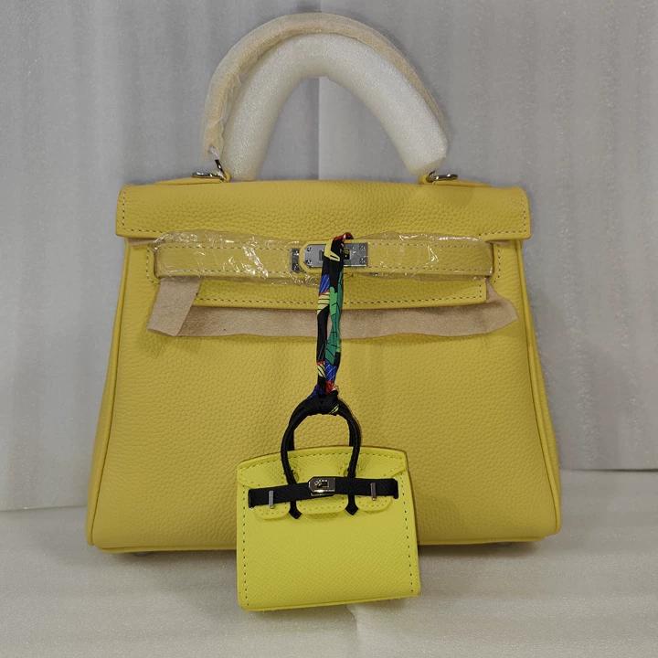 Yellow mini Birkin bag charm with black straps hanging on a matching yellow leather handbag.