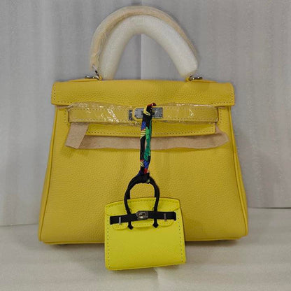 Yellow mini Birkin bag charm with black straps hanging on a matching yellow leather handbag.
