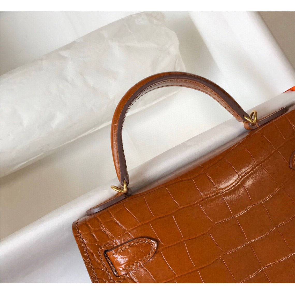 Close-up of gold brown croc embossed leather mini Kelly handbag showing sturdy top handle and luxury grain.