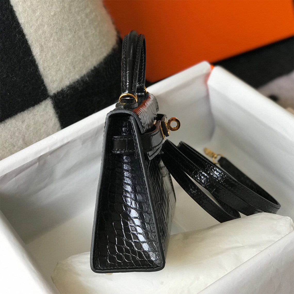 Side view of black croc embossed leather mini Kelly bag with gold hardware and removable strap.