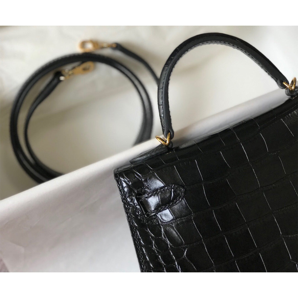 Close-up of black croc embossed leather mini Kelly handbag with top handle and shoulder strap.