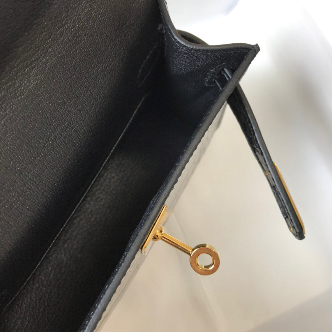 Interior view of black mini Kelly bag showing faux leather lining and gold-tone turn-lock hardware.