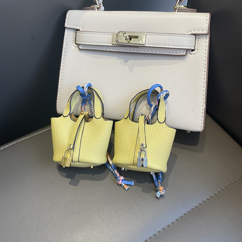 Yellow mini leather Picotin bag charms with silk ribbon on white handbag.