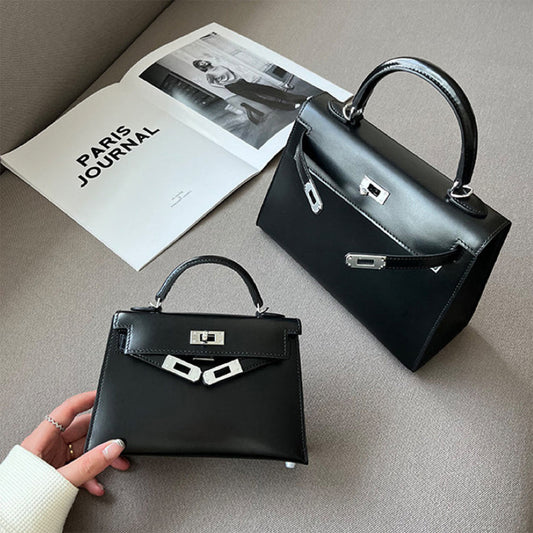 Two classic black Box Leather Kelly-style handbags in Mini and Large sizes, featuring a structured Sellier silhouette and silver hardware, displayed next to a "Paris Journal" magazine.