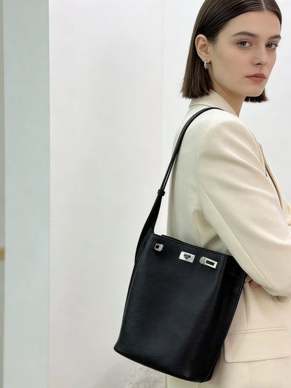 Model wearing a black pebbled top-grain leather Kelly bucket bag as an underarm shoulder bag with a cream blazer.