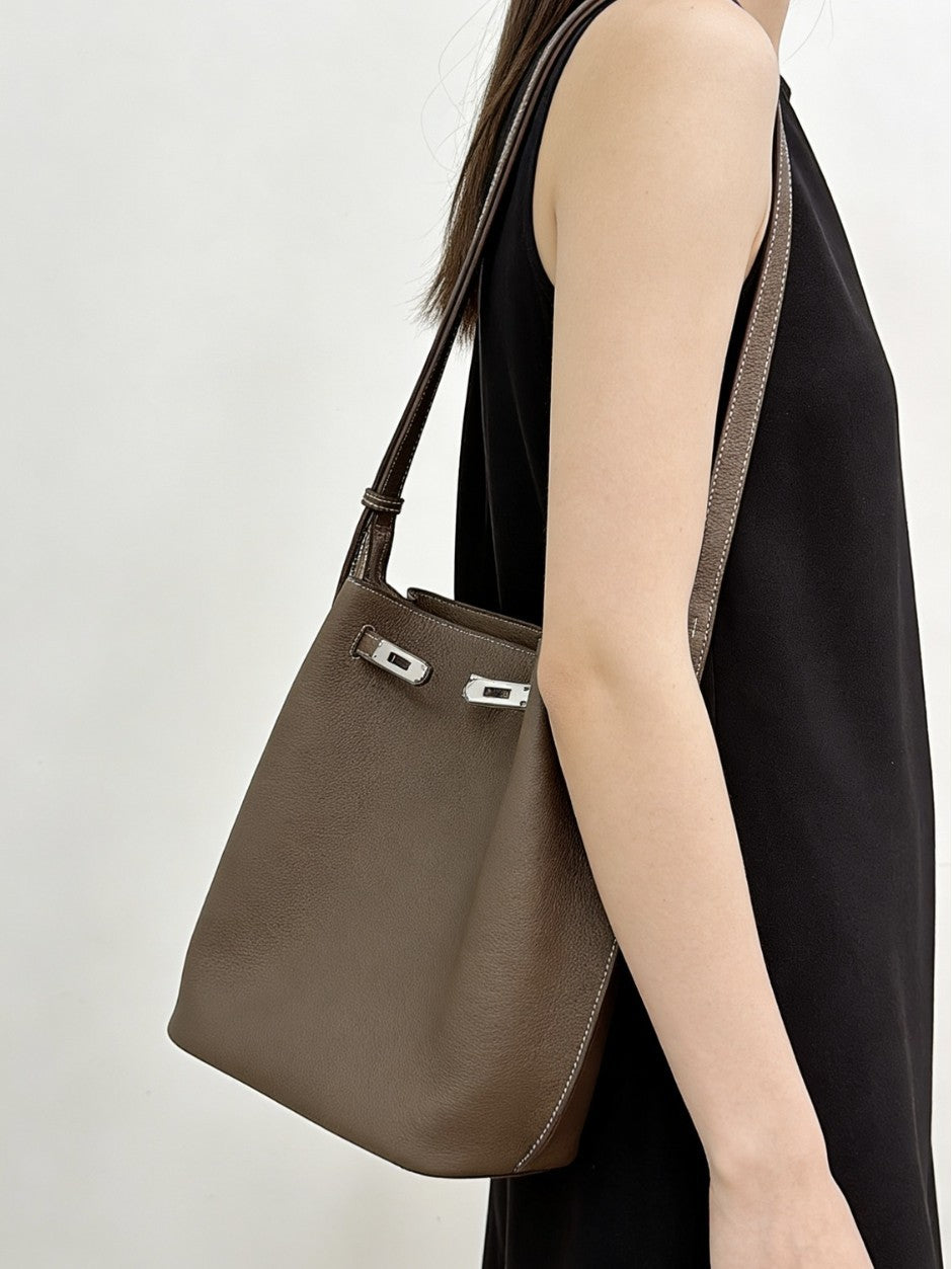 Taupe pebbled top-grain leather Kelly bucket bag worn as an underarm shoulder bag with a black sleeveless dress.