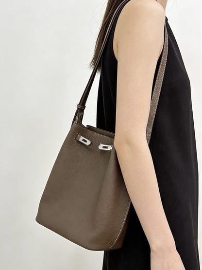 Taupe pebbled top-grain leather Kelly bucket bag worn as an underarm shoulder bag with a black sleeveless dress.