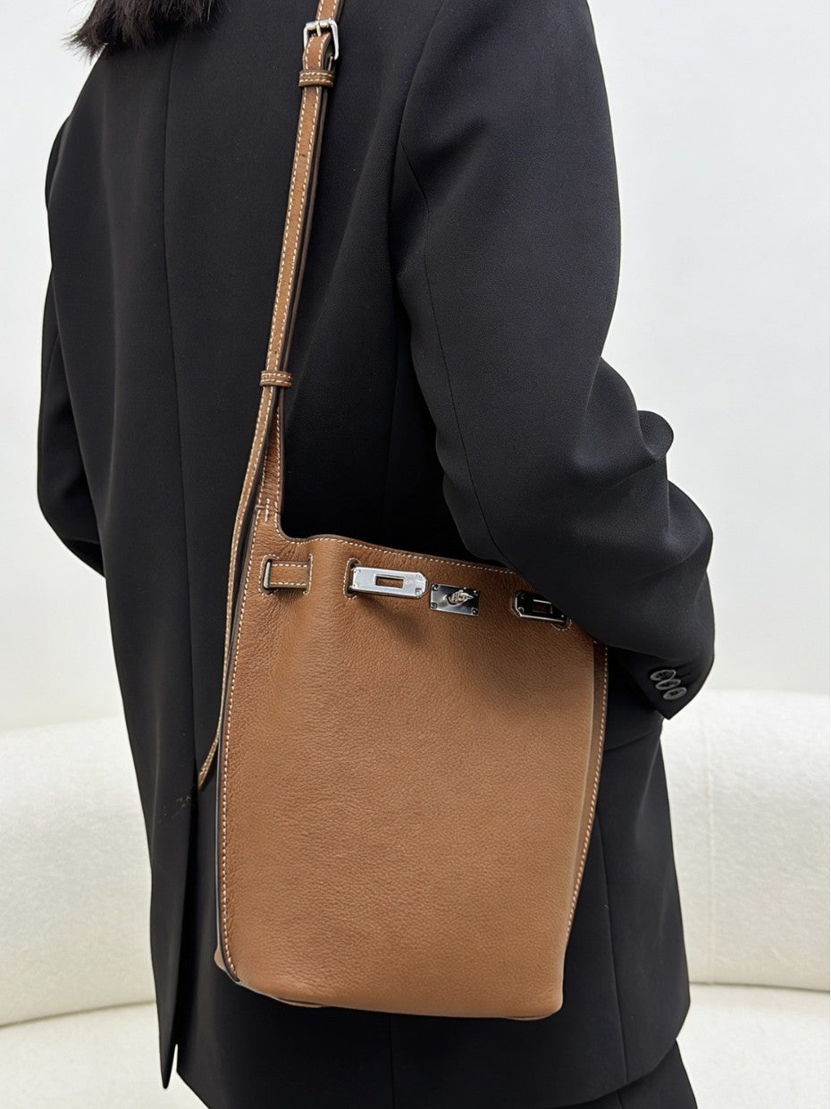 Brown pebbled top-grain leather Kelly bucket bag with adjustable shoulder strap and silver hardware worn with a black blazer.