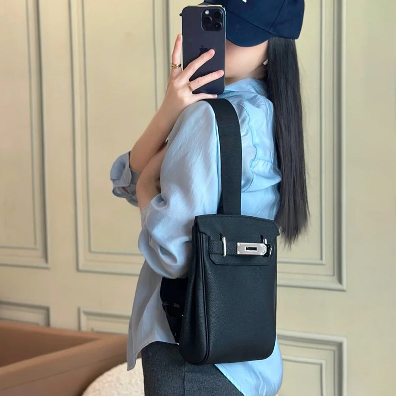 A model wearing the Unisex Togo FannyPack in black, styled as a crossbody backpack over a blue denim shirt to demonstrate its size and adjustable wide strap.
