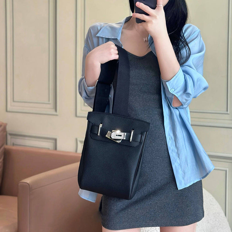 A model holding the black Unisex Togo FannyPack as a handbag, showcasing its top grain leather texture and silver turn-lock closure against a blue shirt and grey dress.