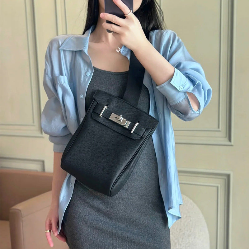 A model wearing a black Unisex Togo FannyPack as a high-chest crossbody backpack, styled with a blue button-down shirt and grey dress to show its versatile, luxury look.
