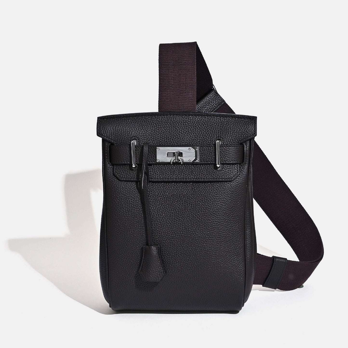 Front view of the Ebene Unisex Togo FannyPack in pebbled top grain leather, featuring a silver turn-lock closure and a wide black fabric crossbody strap.
