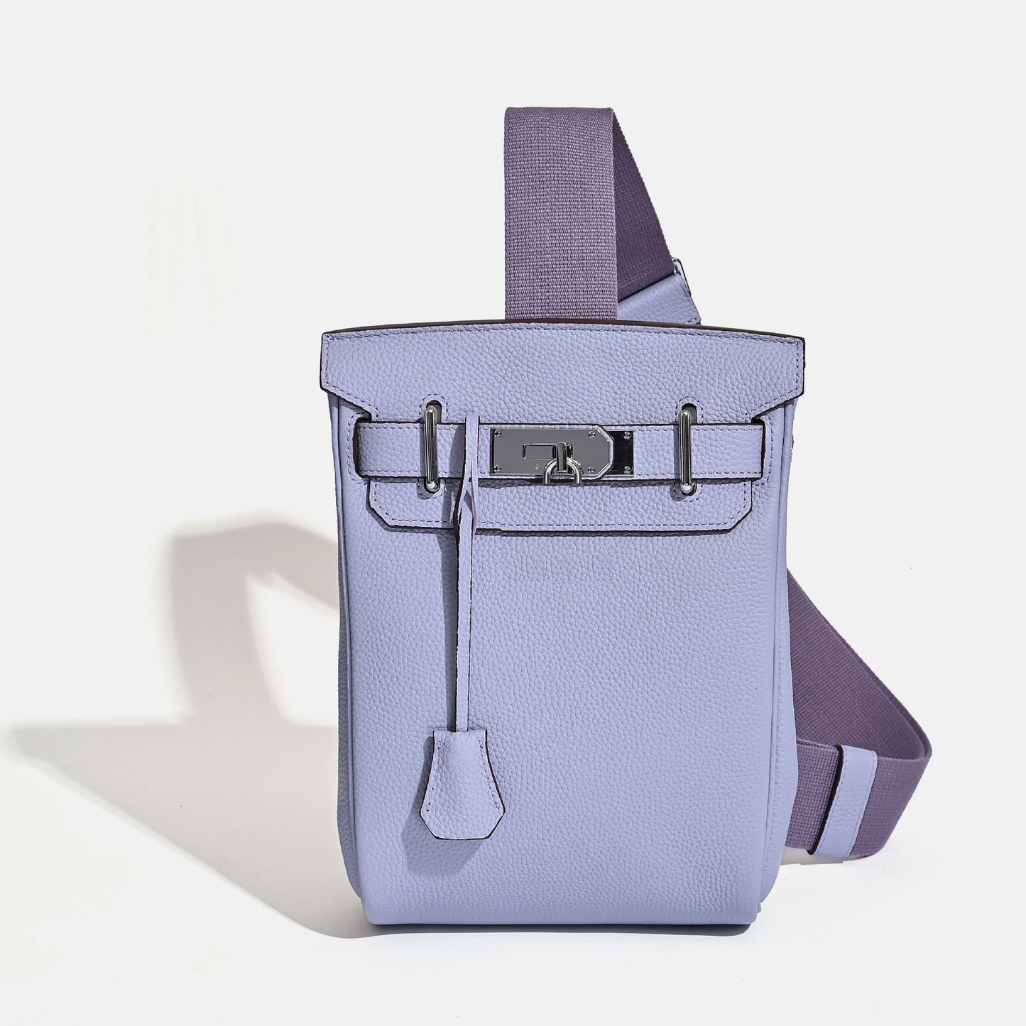 Front view of the Light Purpel Unisex Togo FannyPack in pebbled top grain leather, featuring a silver turn-lock closure and a wide black fabric crossbody strap.