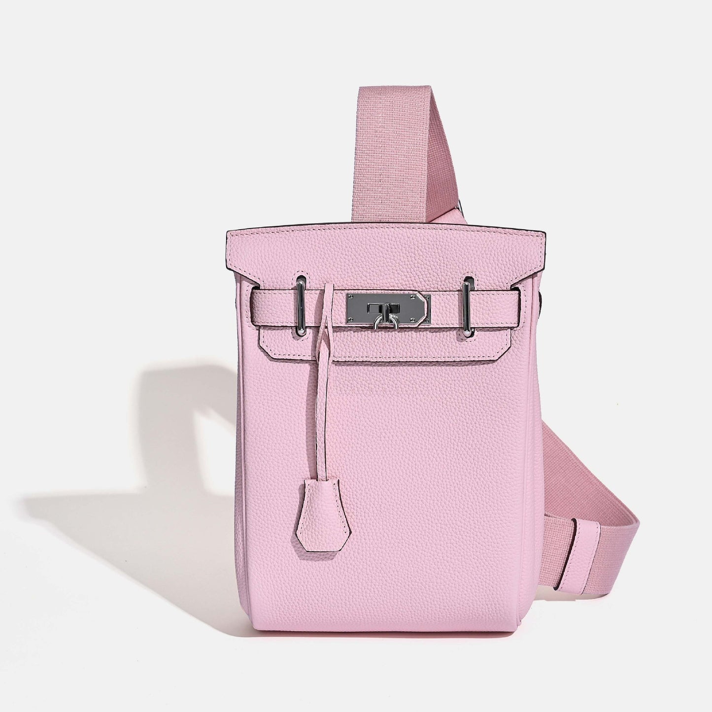 Front view of the Pink Unisex Togo FannyPack in pebbled top grain leather, featuring a silver turn-lock closure and a wide black fabric crossbody strap.
