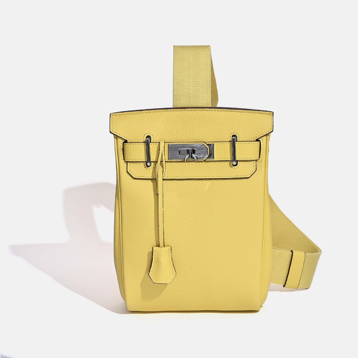 Front view of the Yellow Unisex Togo FannyPack in pebbled top grain leather, featuring a silver turn-lock closure and a wide black fabric crossbody strap.