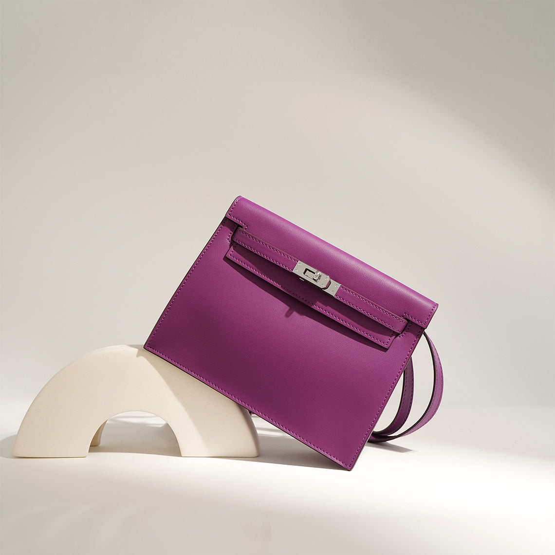 An elegant purple top grain leather Kelli Danse shoulder bag with silver hardware, displayed on a minimalist artistic stand.