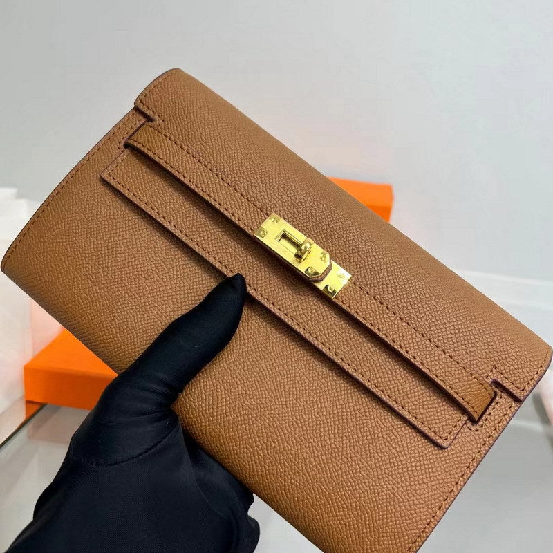 Close-up of a tan inspired Kelli long wallet held in a gloved hand, showcasing the premium textured cowhide leather and iconic golden Kelly closure.