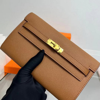 Close-up of a tan inspired Kelli long wallet held in a gloved hand, showcasing the premium textured cowhide leather and iconic golden Kelly closure.