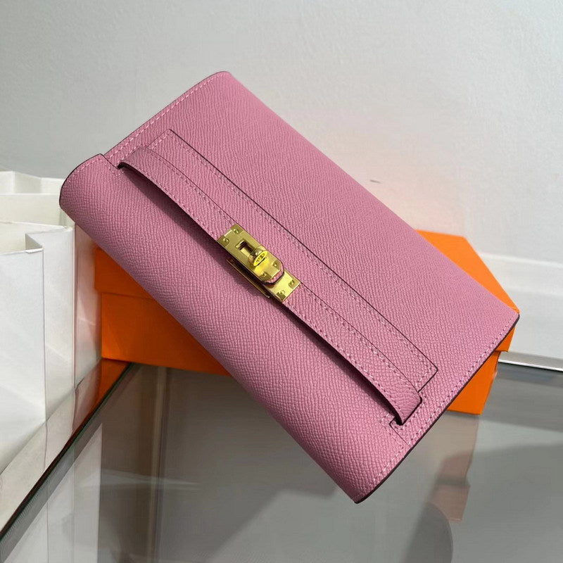 Angled view of a pink inspired Kelly to go wallet in textured cowhide leather, featuring the iconic golden Kelly closure and signature orange packaging in the background. 