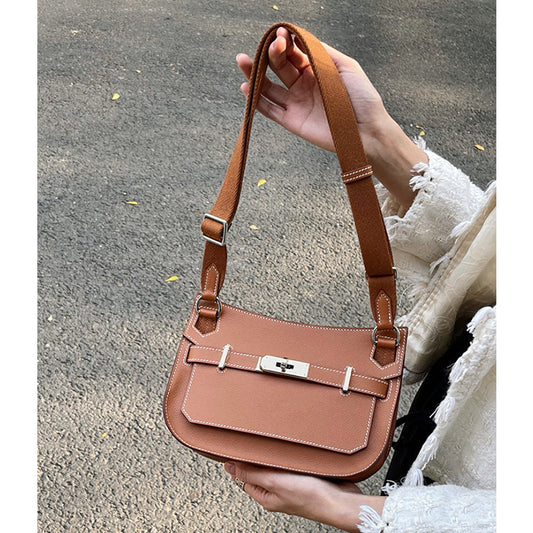 A Golden Brown leather Gypsy shoulder bag with white contrast stitching and an adjustable strap, held outdoors to show its unisex messenger style.