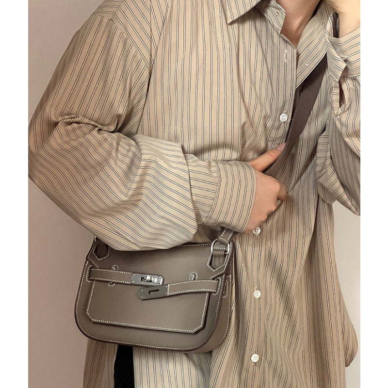 An Etoupe leather Gypsy crossbody bag with white contrast stitching styled over an oversized striped shirt, showcasing a sophisticated unisex look.